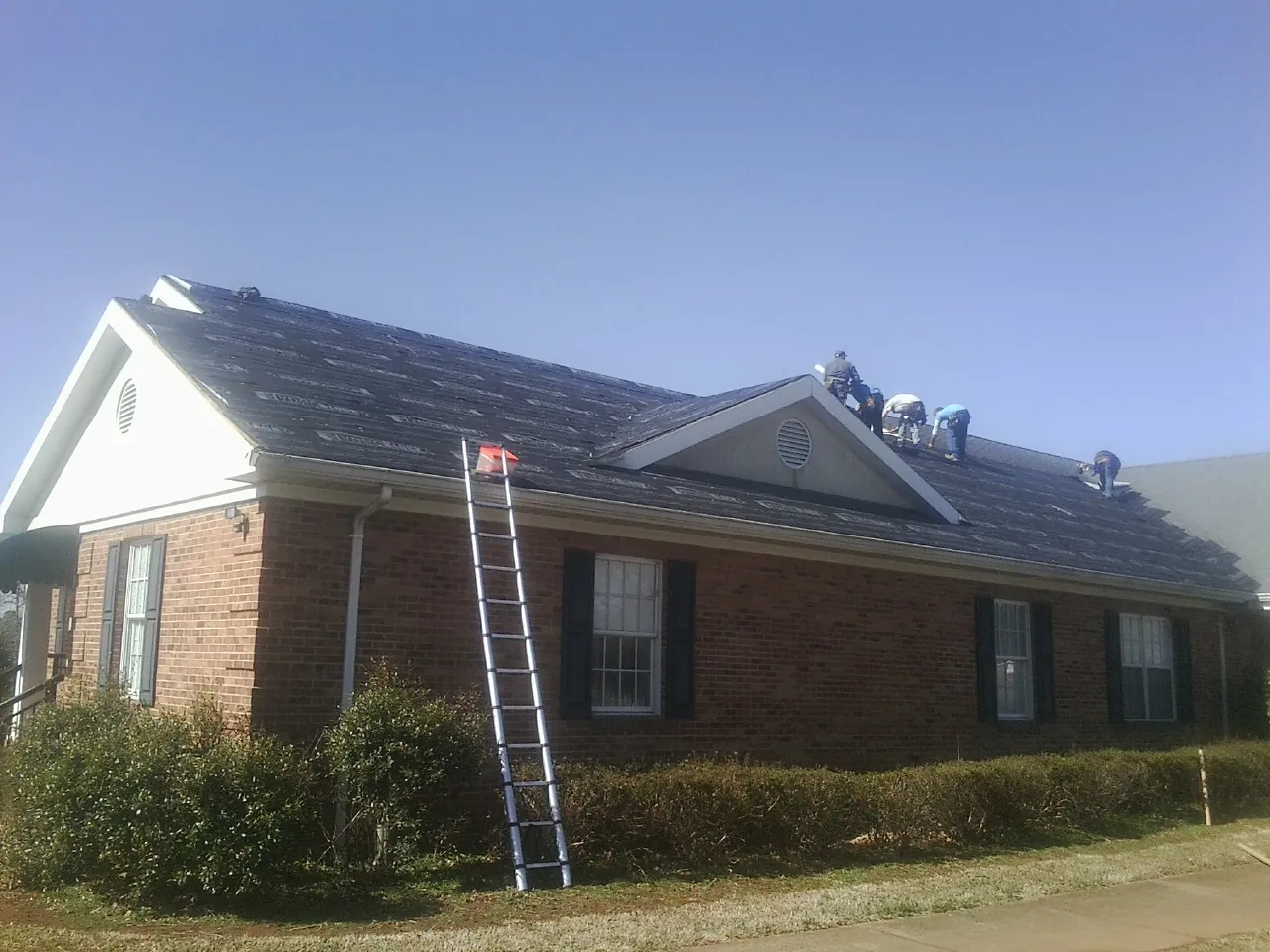 Crew tearing shingles off a brick ranch roof with a ladder set — Emergency Roof Repair work by our crew in Holbrook