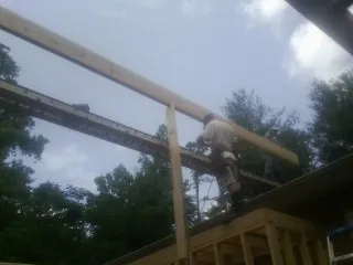 Carpenter setting a ridge beam over a new addition frame in Holbrook
